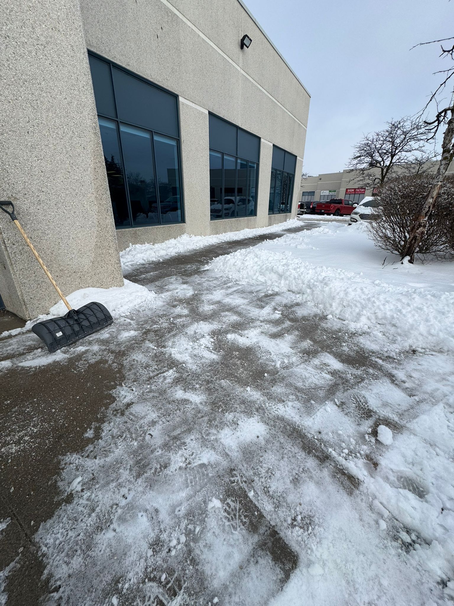 Snow shovel resting on a partially cleared walkway